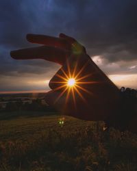 Silhouette hand on field against sky during sunset