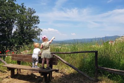 Siblings standing on bench against sky