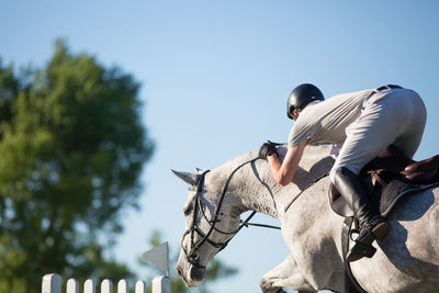 Low section of jockey jumping horse against sky