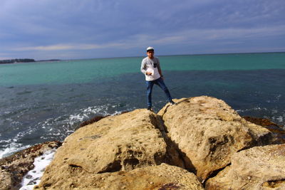 Man standing on rock at beach against sky