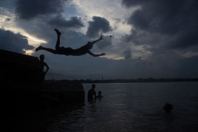 Silhouette people by sea against sky during sunset