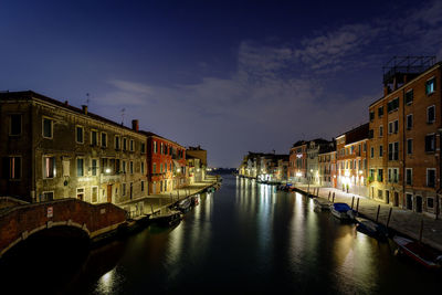 Canal amidst illuminated buildings in city at night