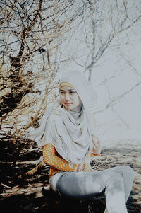 Portrait of young woman sitting on snow covered bare tree