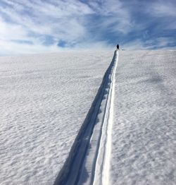 Ski track leading towards person standing snowcapped mountain against cloudy sky