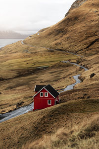 Narrow countryside road and small cottage located on coast of calm sea on cloudy day on faroe islands