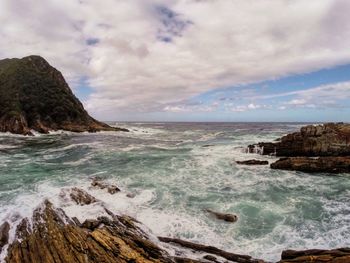 Rock formations by sea at tsitsikamma national park against cloudy sky