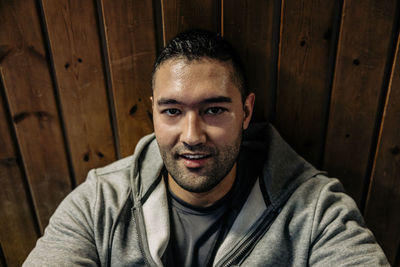 Portrait of male athlete relaxing while sitting in front of wooden wall