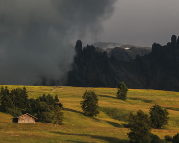 Mountain madow at dunstest with trees and cabin against dark stormy sky