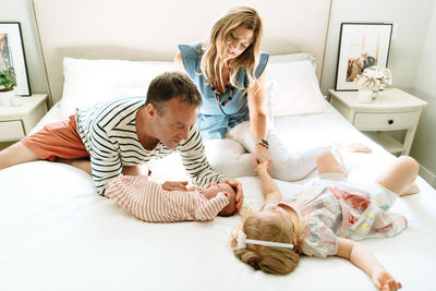 A mother and father sitting on a bed together with their daughters