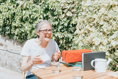 Portrait of young woman using mobile phone while sitting against plants