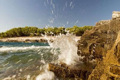 Waves splashing on rocks against sky