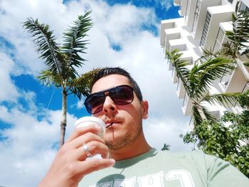 Man sucking drink against cloudy sky