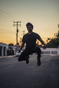 Full length of man jumping on street against sky during sunset