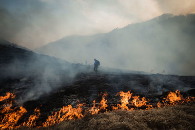 Man standing by bonfire on mountain against sky