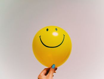 Close-up of hand holding yellow balloon against white background