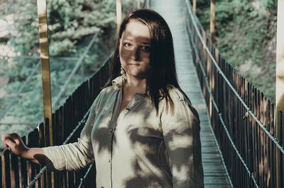 Portrait of young woman standing by railing