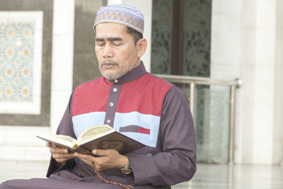 Mature man reading koran while sitting at mosque