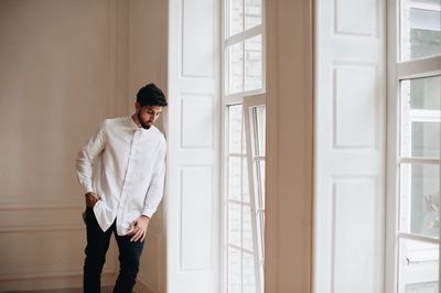 Young man looking away while standing against wall