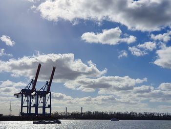 Cranes by sea against sky