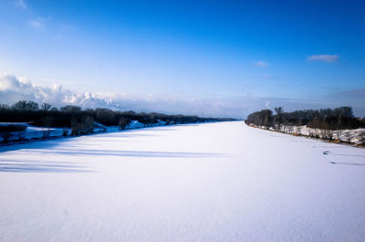 Snow covered field by lake against blue sky