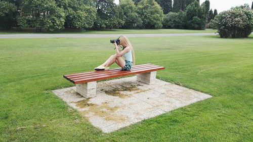 Woman photographing while sitting on bench at park