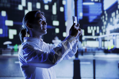 Side view of man photographing with arms raised in city