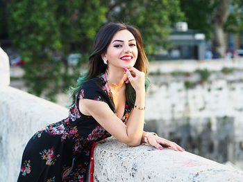 Portrait of beautiful woman smiling while leaning on retaining wall