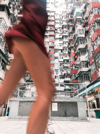 Low section of man walking on street amidst buildings in city