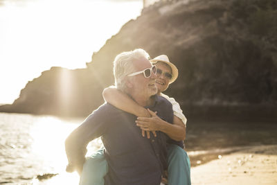 Senior man piggybacking woman at beach during sunny day