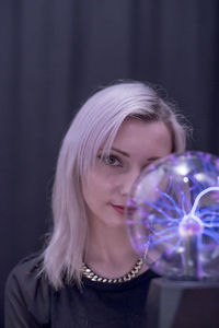 Close-up portrait of young woman holding plasma ball over black background