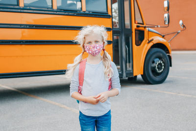  caucasian girl student wearing face mask near yellow bus.  education and back to school. new normal. 