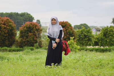 Portrait of smiling woman in hijab standing on field 