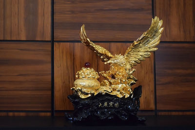 Golden bird shaped decoration on table by wooden wall