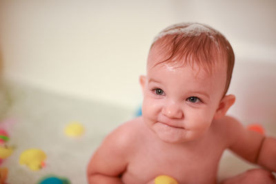 High angle view of cute wet baby girl looking away while sitting in bathtub at home