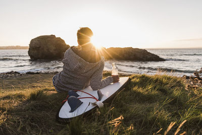 France, bretagne, crozon peninsula, woman sitting at the coast at sunset with surfboard