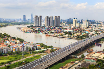 High angle view of bridge and buildings in city against cloudy sky on sunny day