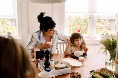 Mother looking at daughter having breakfast on dining table