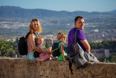 Side view of friends sitting on rock against sky