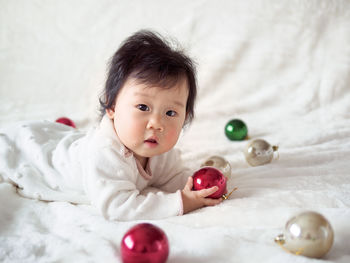 Portrait of cute baby girl lying on bed with christmas ornaments at home