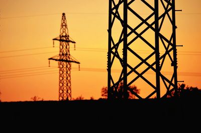 Low angle view of silhouette electricity pylon against orange sky