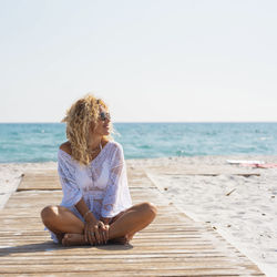 Woman sitting at beach against clear sky