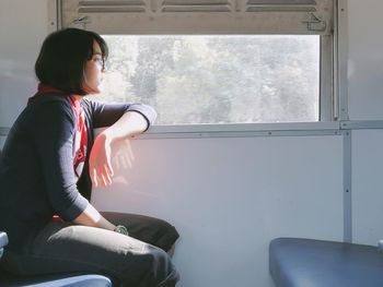 Side view of young woman sitting by window in train