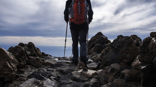 Low section of man standing on rock against sky