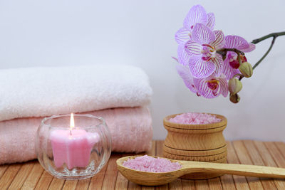 Candle with salts and flowers by towel on table