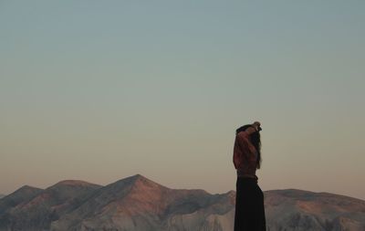 Rear view of woman standing on mountain against clear sky