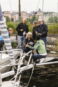 Senior men and women listening to female instructor by yacht during boat master course