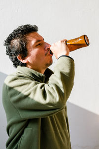 Side view of man drinking beer standing against wall