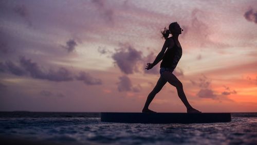 Silhouette of woman practicing yoga at sea