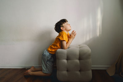 A boy in an orange t-shirt prays at home. concept for faith