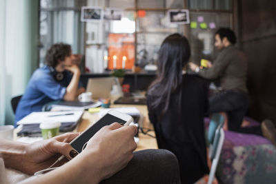 Close-up of woman holding mobile phone against colleagues working in creative office